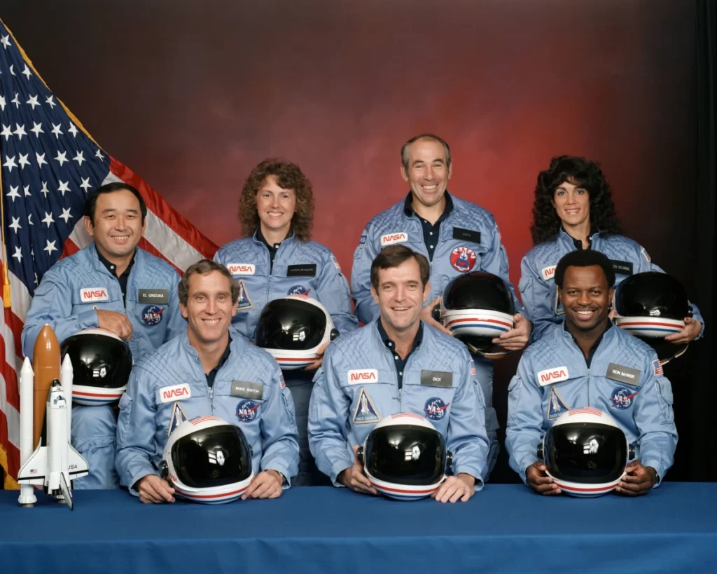 I membri dell'equipaggio dell'STS-51L (Challenger) sono:  Ellison S. Onizuka, Sharon Christa McAuliffe, Greg Jarvis, Judy Resnik. In prima fila da sinistra a destra: Mike Smith, Dick Scobee e Ron McNair. 
