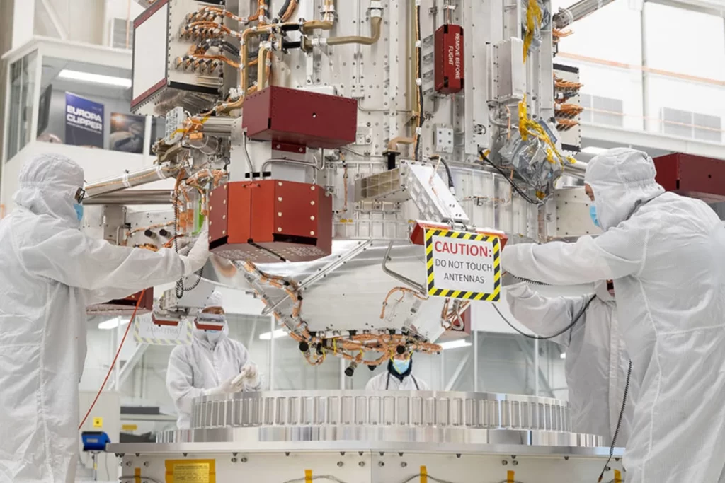 Ingegneri e tecnici utilizzano una gru per posizionare il nucleo della navicella spaziale Europa Clipper della NASA nella camera bianca High Bay 1 della Spacecraft Assembly Facility del Jet Propulsion Laboratory. 
