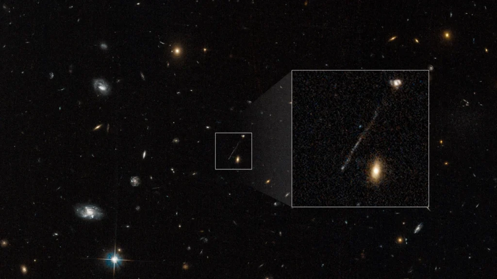 Questa foto d'archivio del telescopio spaziale Hubble cattura un segno lineare che che è stata liquidata per la prima volta come un artefatto di imaging dalle fotocamere di Hubble. Le successive osservazioni rivelano che si tratta di una catena di giovani stelle blu lunga 200.000 anni luce. Il buco nero supermassiccio si trova sulla punta in basso a sinistra, espulso dalla galassia in alto a destra. 